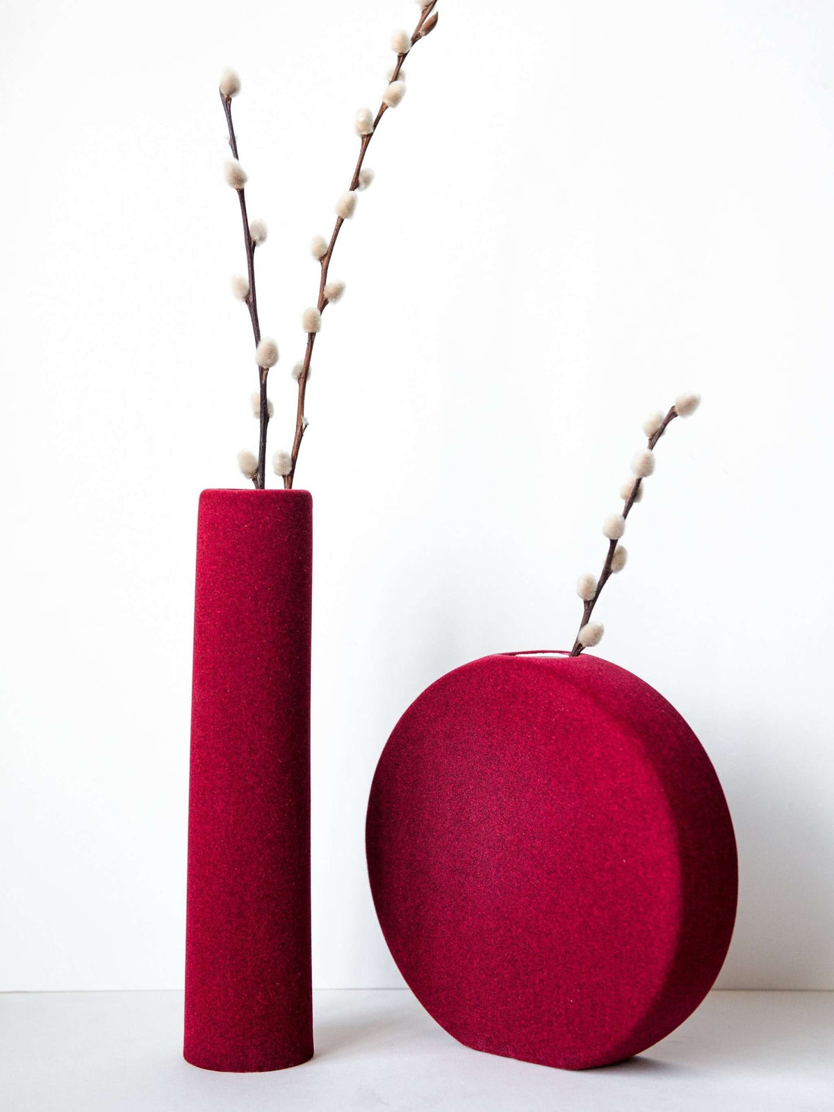 Porcelain set of home decor geometric vases including burgundy tube vase, round vase, and sphere.