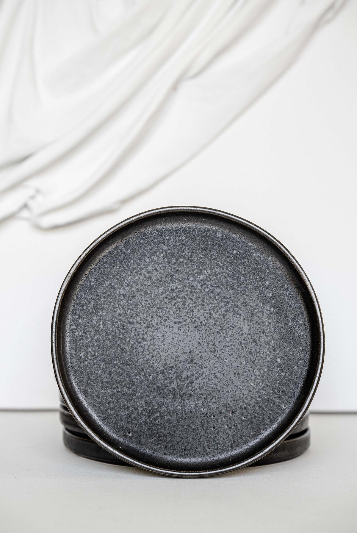 Black stoneware dinner plates with glossy speckled glaze and organic rims on a table setting