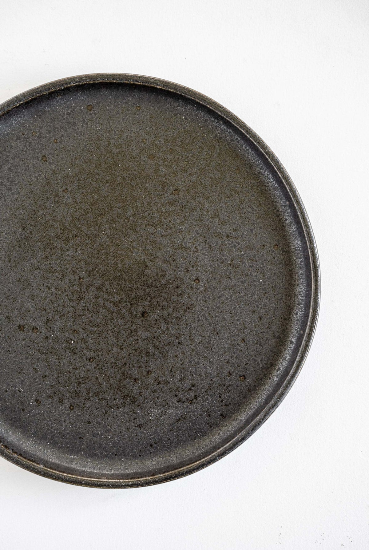 Black stoneware dinner plates with glossy speckled glaze and organic rims stacked on a table