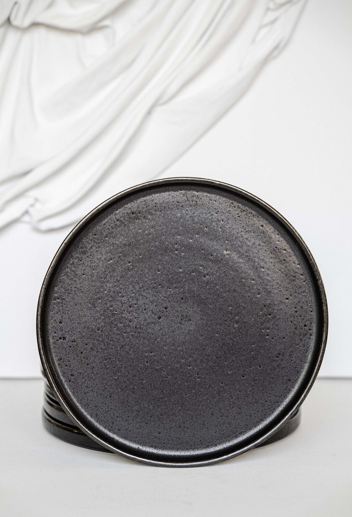 Black stoneware dinner plates with glossy speckled glaze and organic rims on a table setting