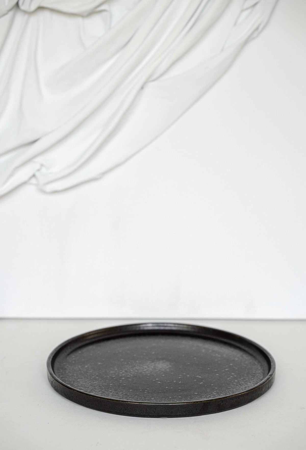 Black stoneware dinner plate with glossy speckled glaze and organic rim detail