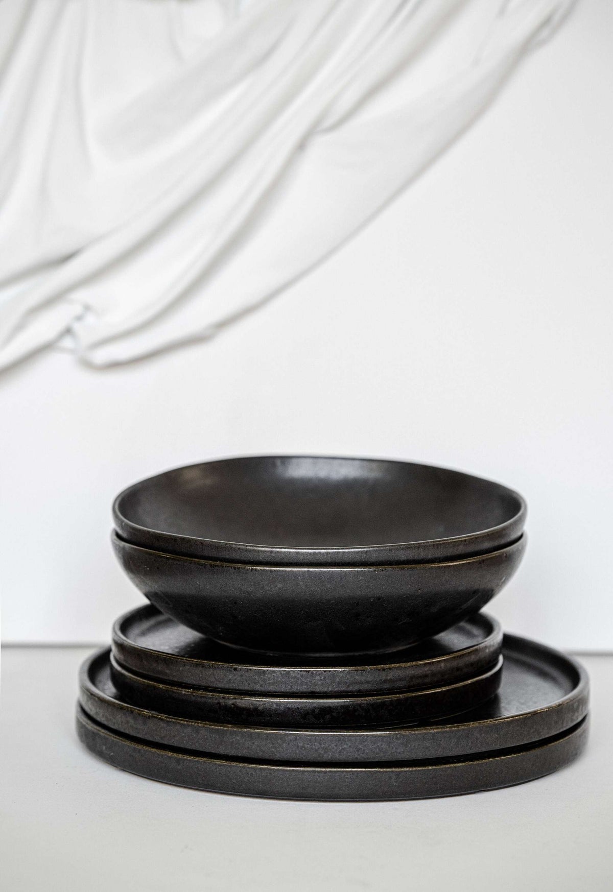 Black stoneware dinner plates with glossy speckled glaze and low edges in modern design