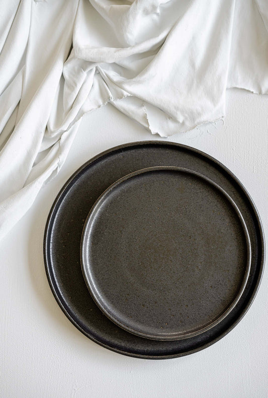 Black stoneware dinner plates with glossy speckled glaze and organic rims