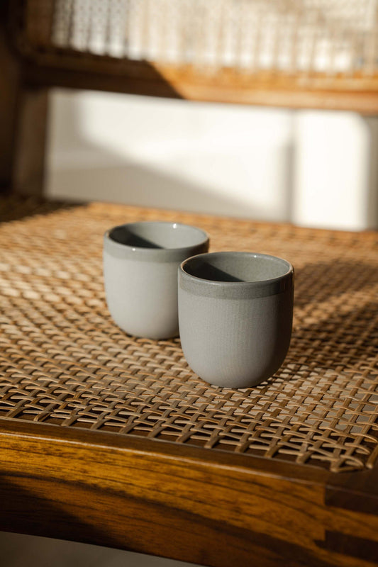 Handmade porcelain espresso cup with shiny glazed interior and exposed clay exterior against gray sky