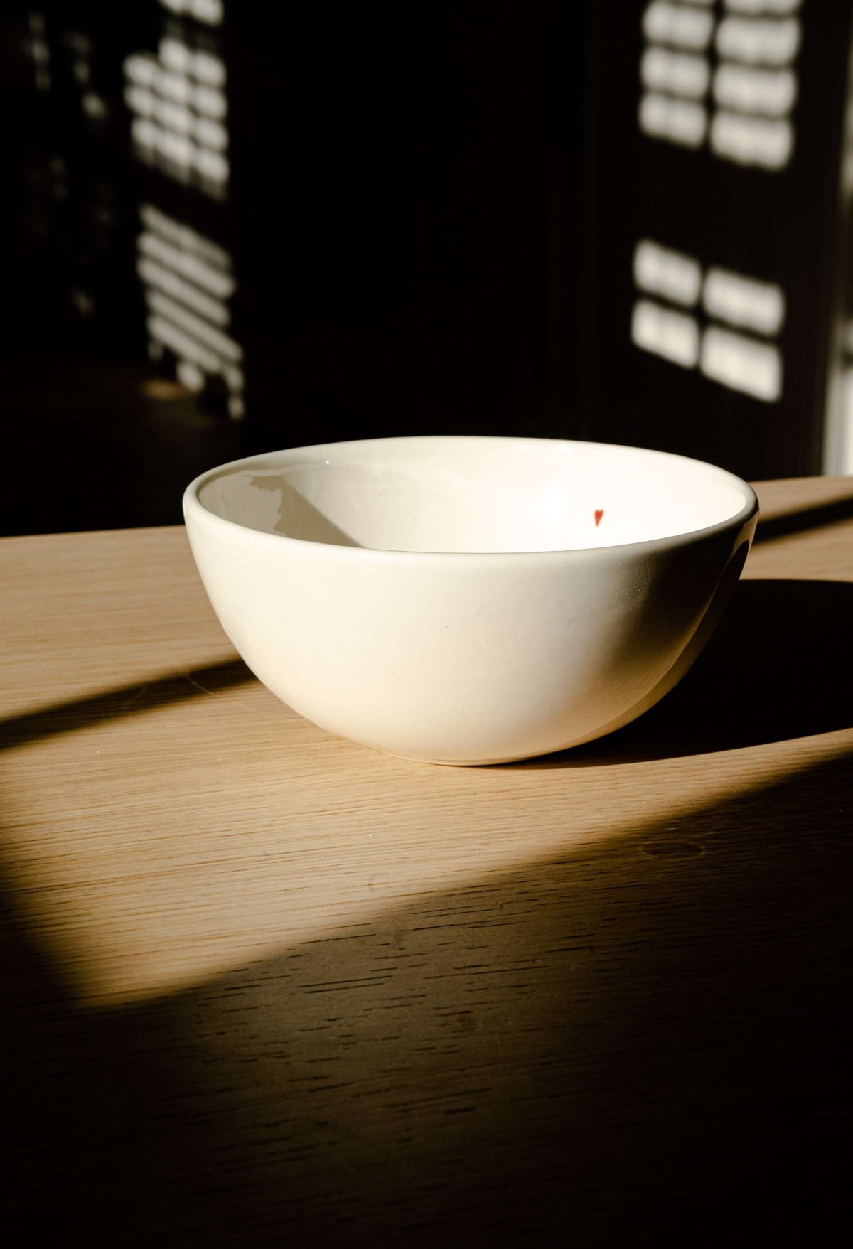 Off-white handmade porcelain bowl with shiny glaze and hand-painted red heart