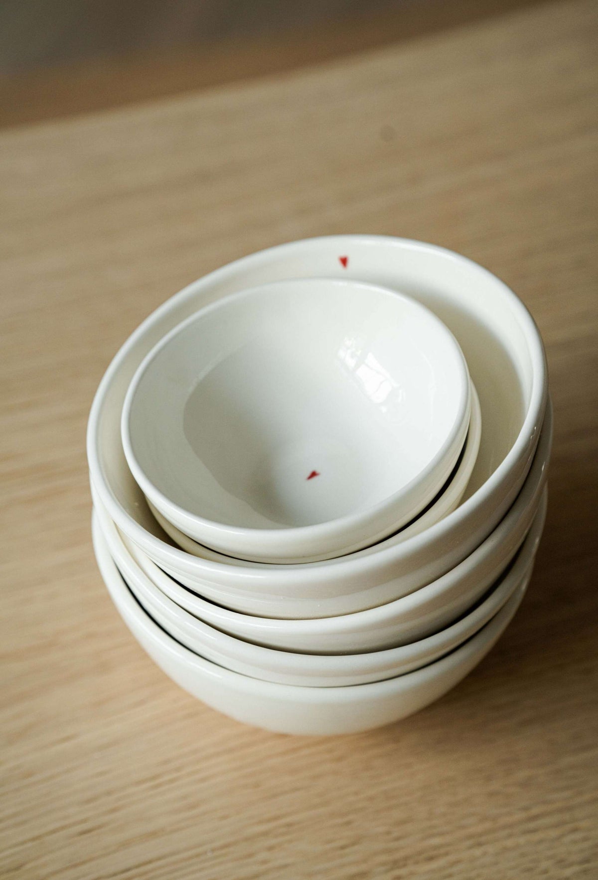 Handmade off-white porcelain bowl with shiny glaze and small red heart detail