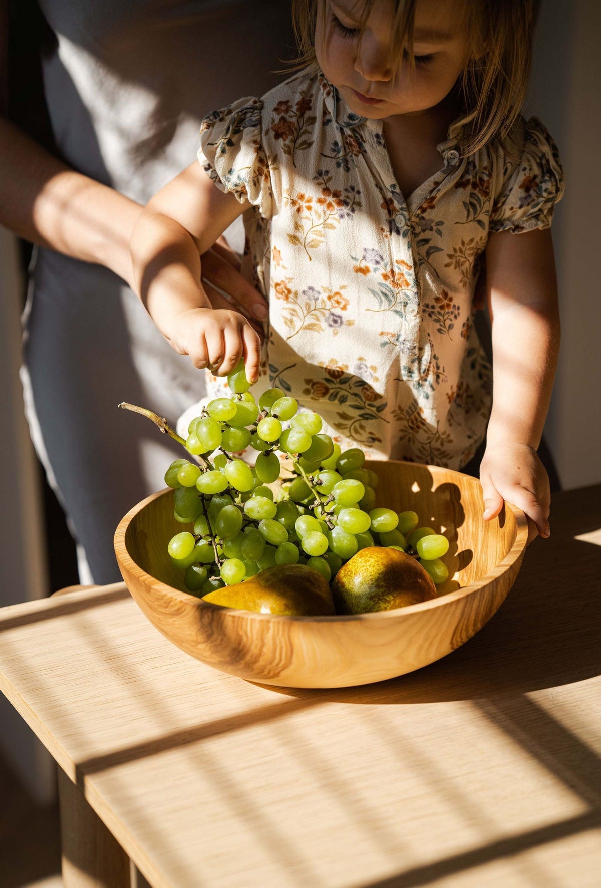 Wooden nesting bowl set featuring a single light-brown wooden bowl with visible grain, filled with green grapes and fruit.