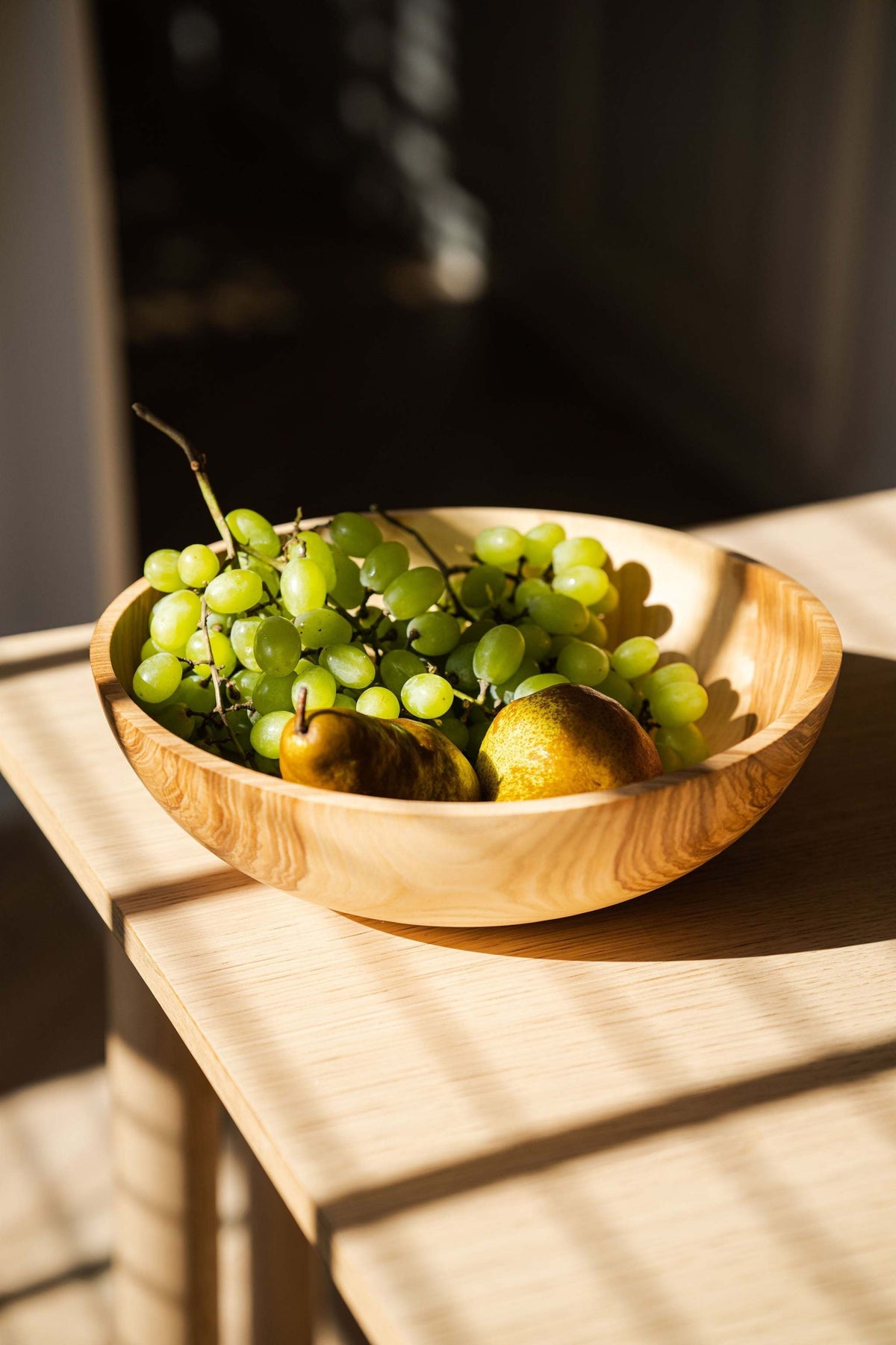 Wooden nesting bowl set with a honey-colored wood grain finish, shown as a wide hand-carved bowl filled with grapes and fruit.