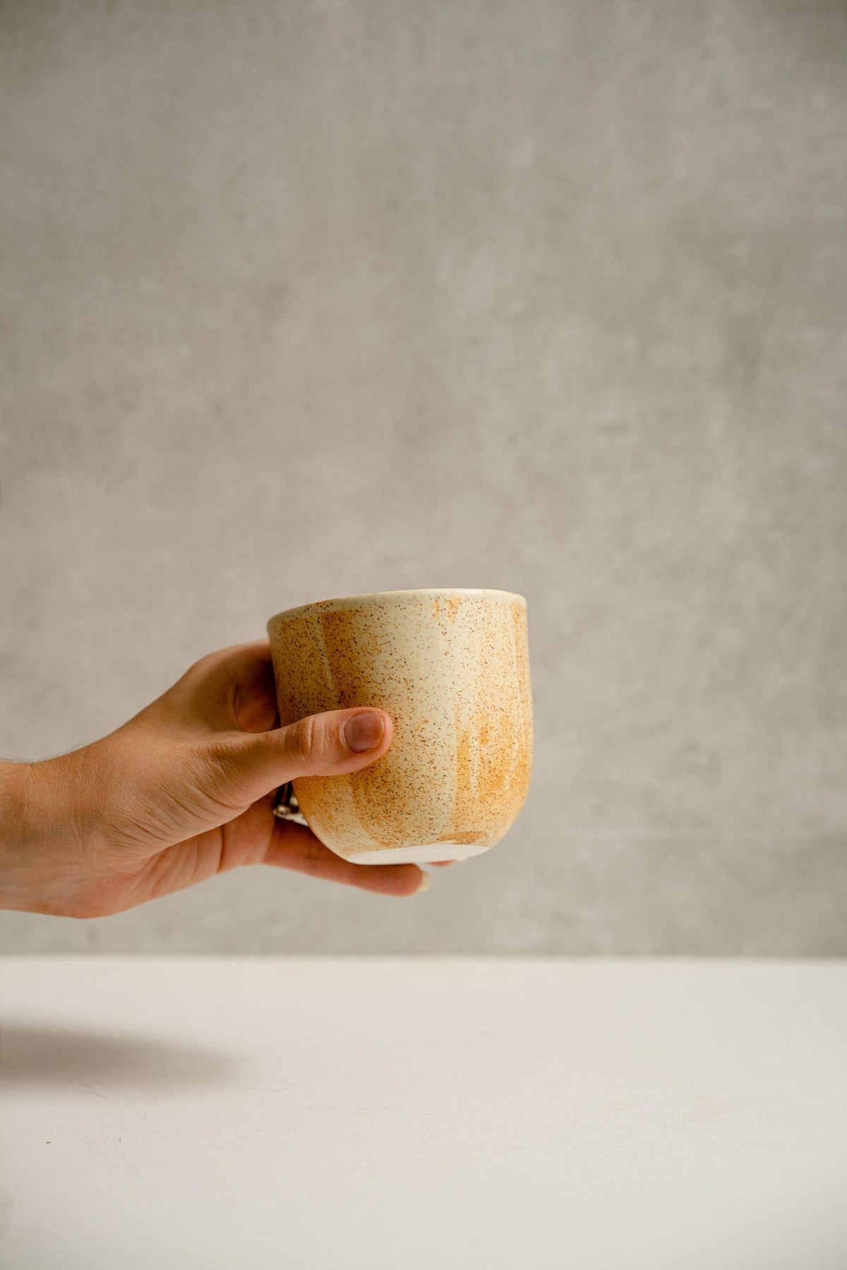 Handmade stoneware beige coffee cup with organic edges and unique reactive glaze swirls