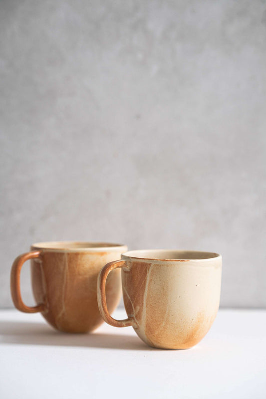 Stoneware beige coffee mug with handle and unique reactive glaze rust drip pattern