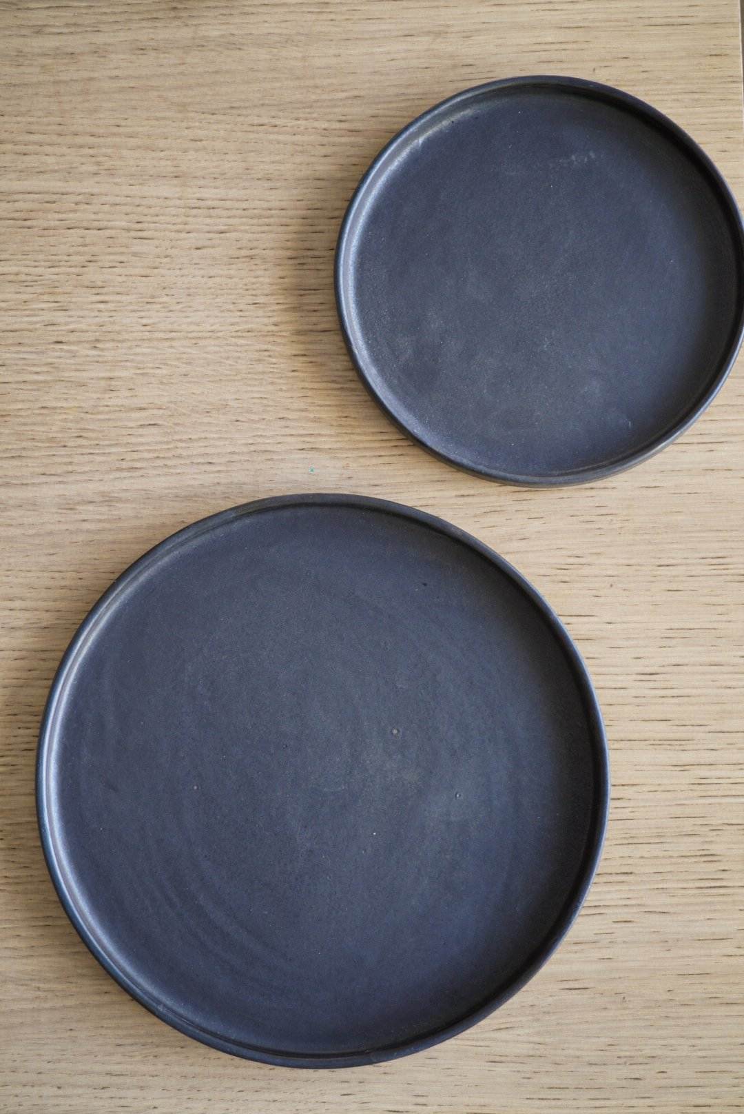Handmade black matte stoneware dinner plate with textured glaze and organic edges, microwave and dishwasher safe.