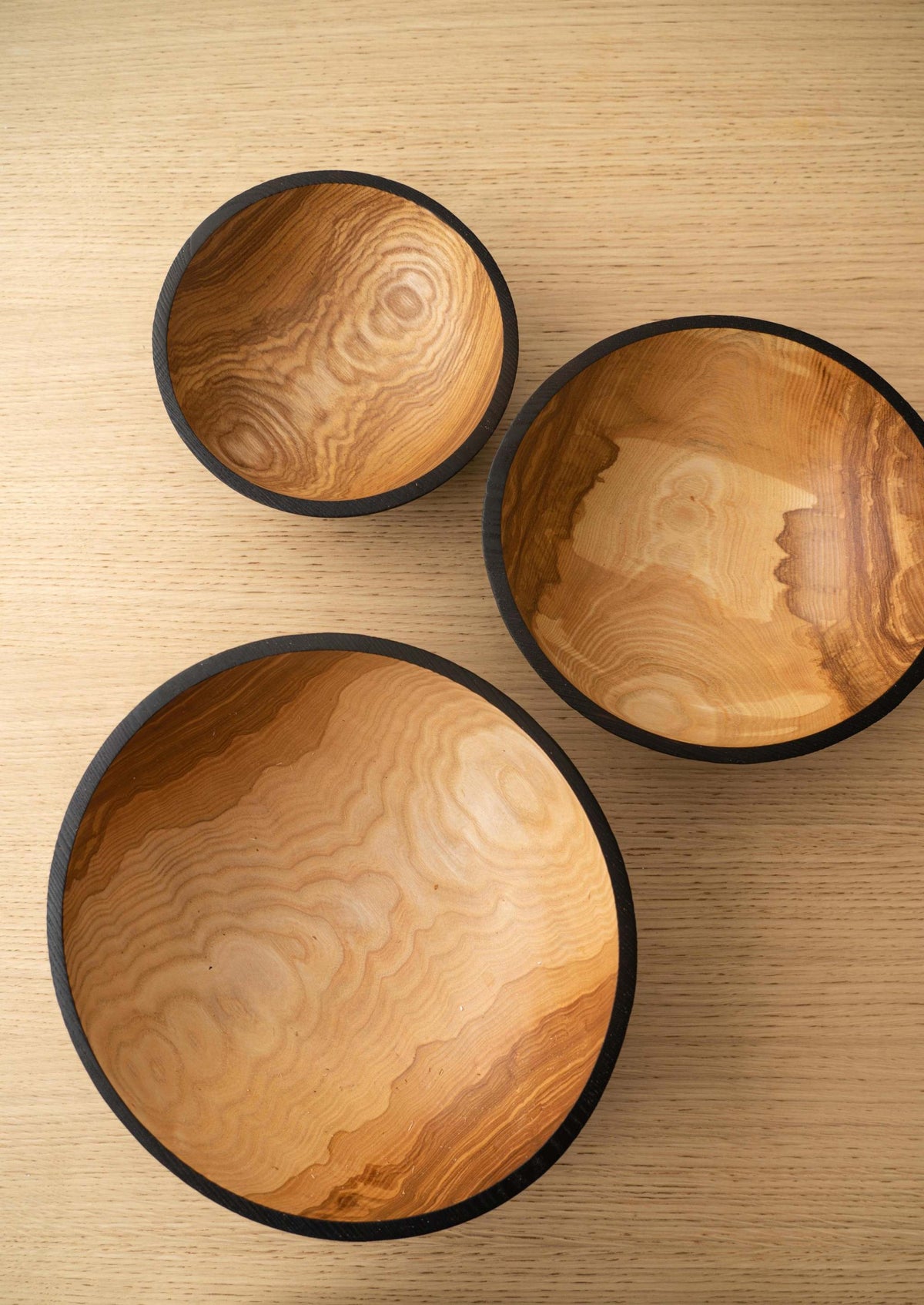 Nesting Bowl Set of three hand-carved ashwood bowls with natural swirling grain, warm brown interiors and charred black rims.