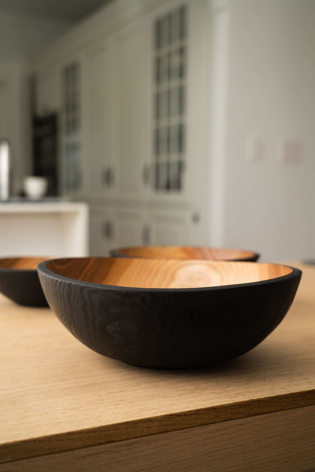 Nesting Bowl Set of three nested wooden bowls with matte black charred exteriors and warm natural wood interiors, showing carved grain.