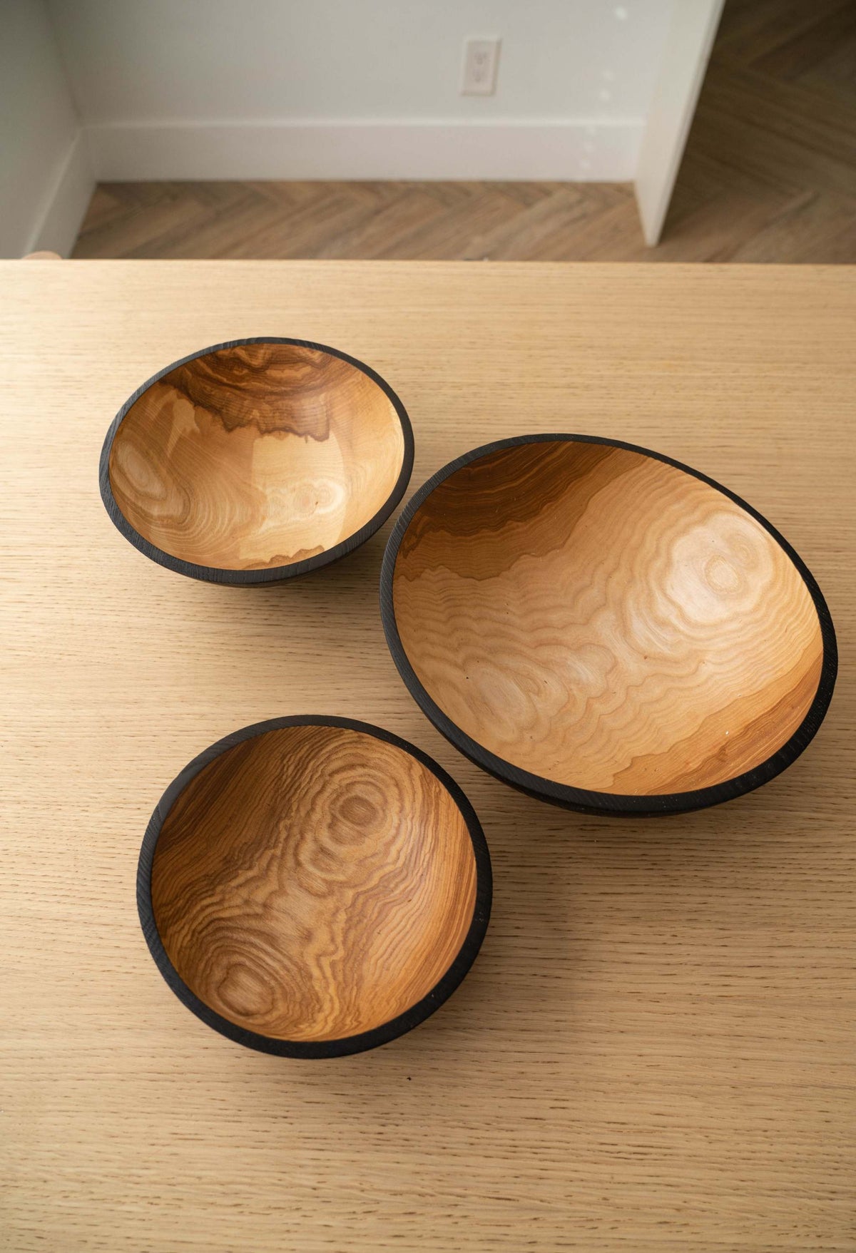 Nesting Bowl Set of three carved ashwood bowls with golden swirling grain and dark charred rims and exteriors.