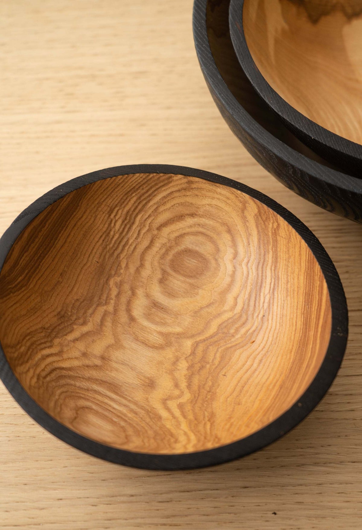 Nesting Bowl Set with natural honey-brown wood grain interiors and distinctive charred black rims, hand-carved from ashwood.