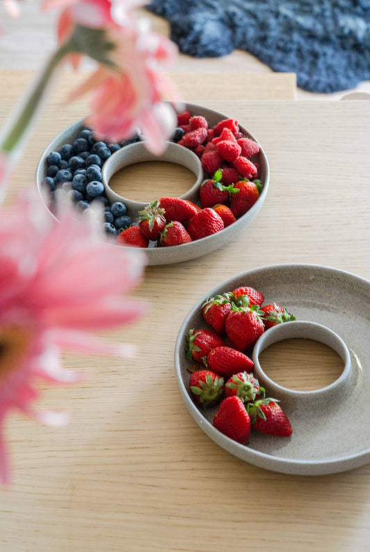 Stoneware serving dish in pale gray speckled ceramic, round with a raised central opening, holding fresh berries
