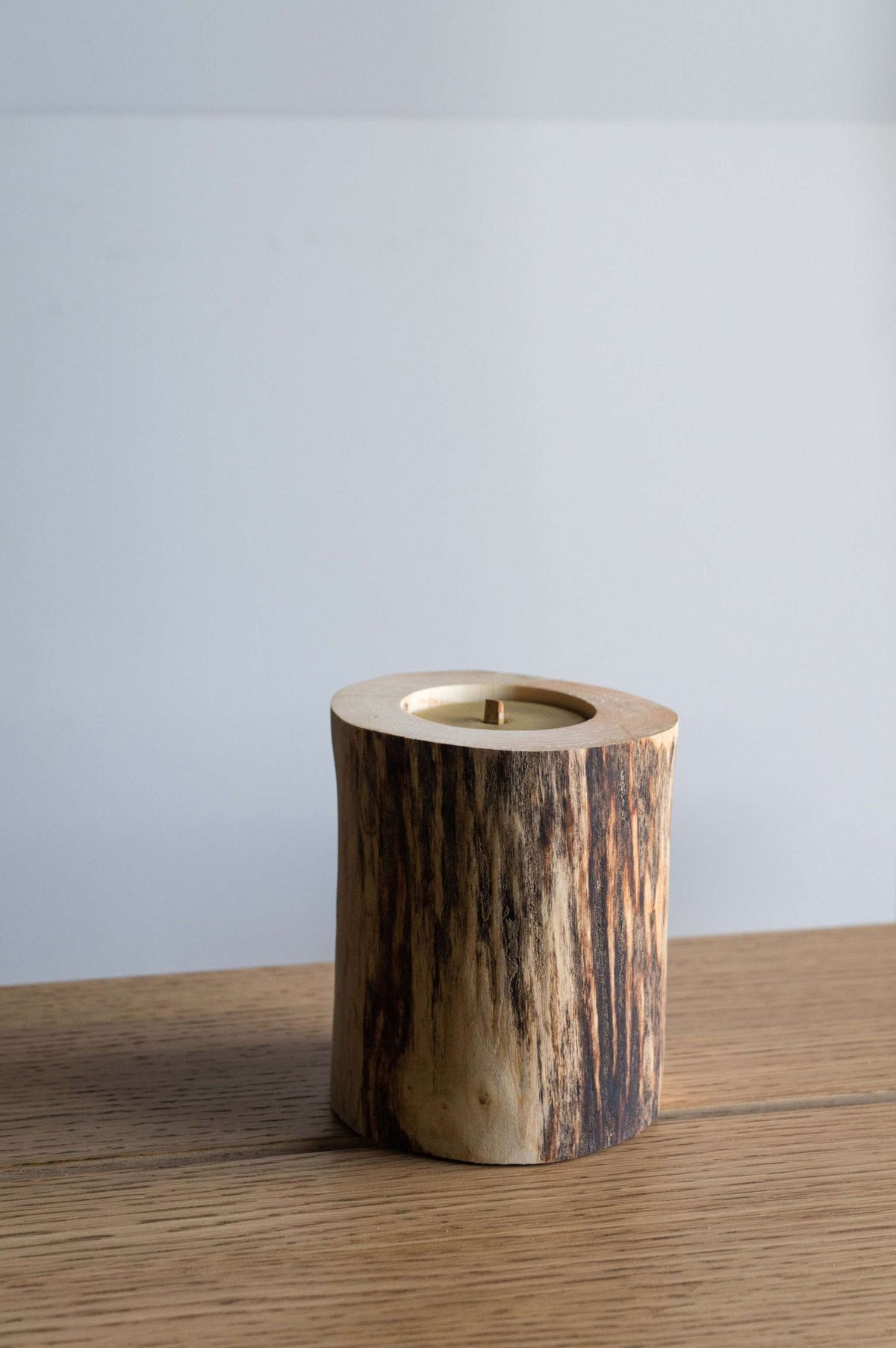 Hand Craft Ubud Wooden Candle in a rustic natural wood holder, with dark bark-like grain and a recessed wax center.