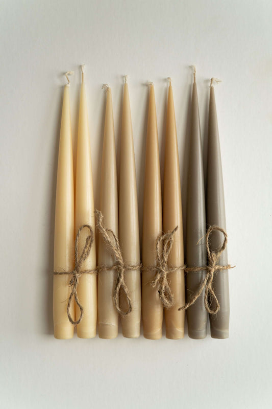 Set of handmade narrow taper candles in glass holders, showcasing earthy colors and warm glow