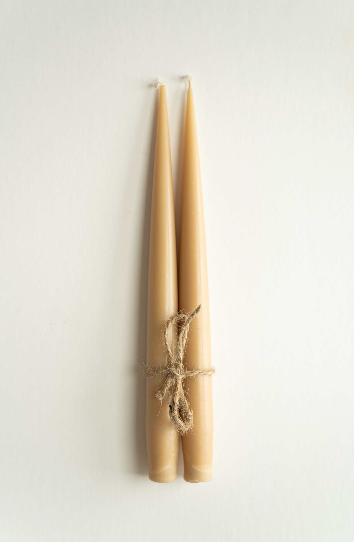 Set of handmade narrow taper candles in four colors, placed in glass holders on a table