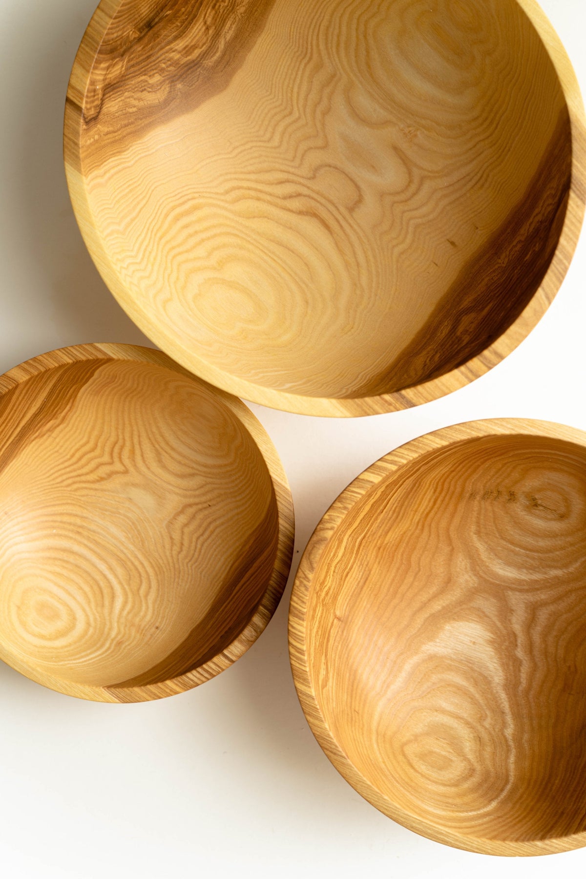 Wooden nesting bowl set in honey-toned wood, with three hand-carved bowls and distinctive flowing grain patterns.