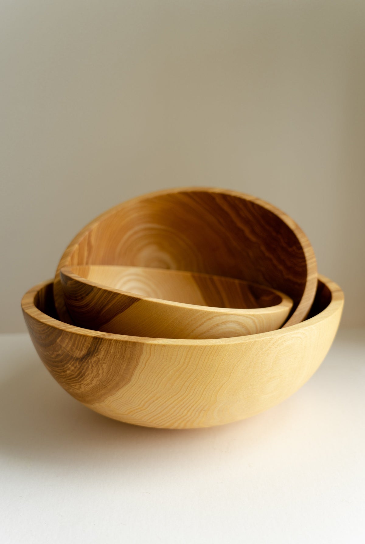 Wooden nesting bowl set in warm golden-brown wood, featuring three hand-carved bowls with swirling natural grain.
