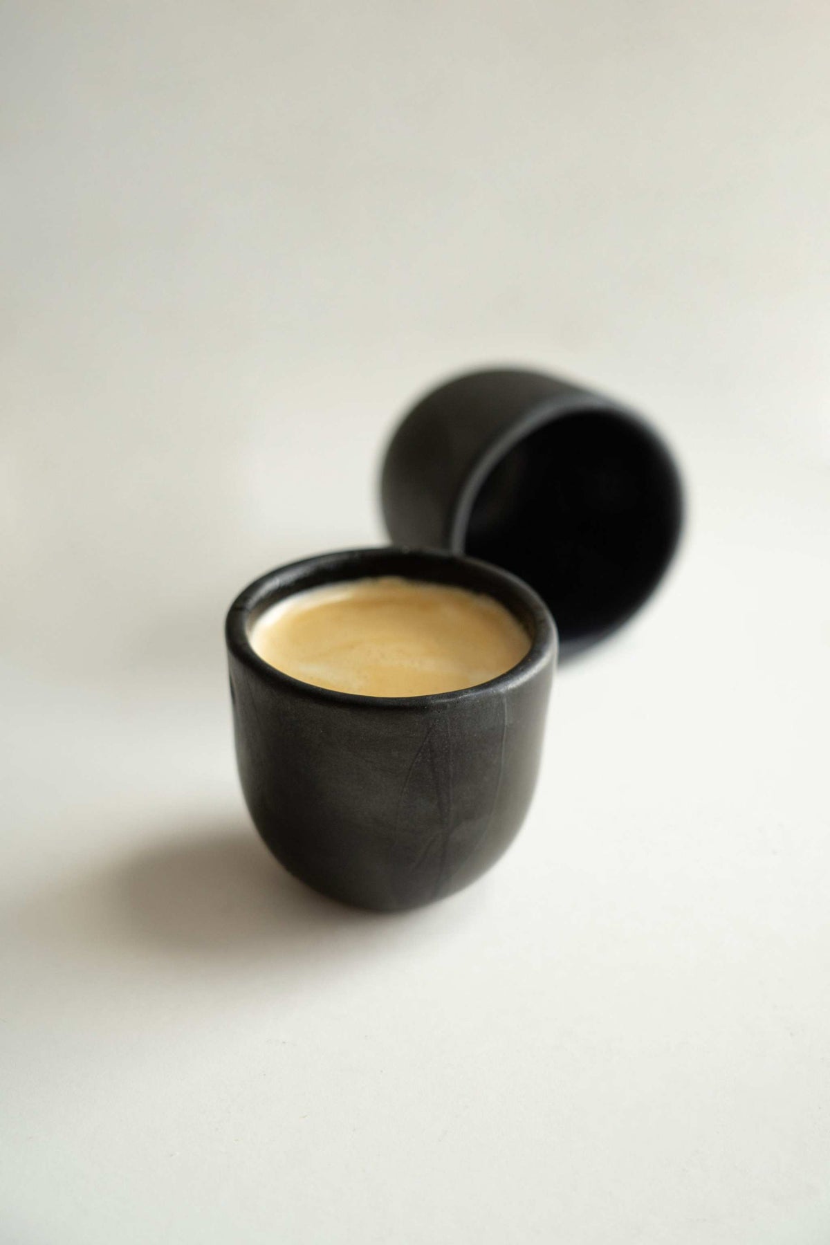 Handmade black stoneware espresso cup with reactive glaze and organic edges