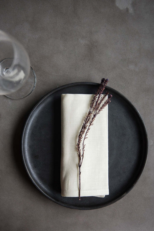 Set of 4 stonewashed organic linen napkins in black, sand, copper, and cream colors with straight hems, soft texture, and casual crinkles, made in Ukraine.
