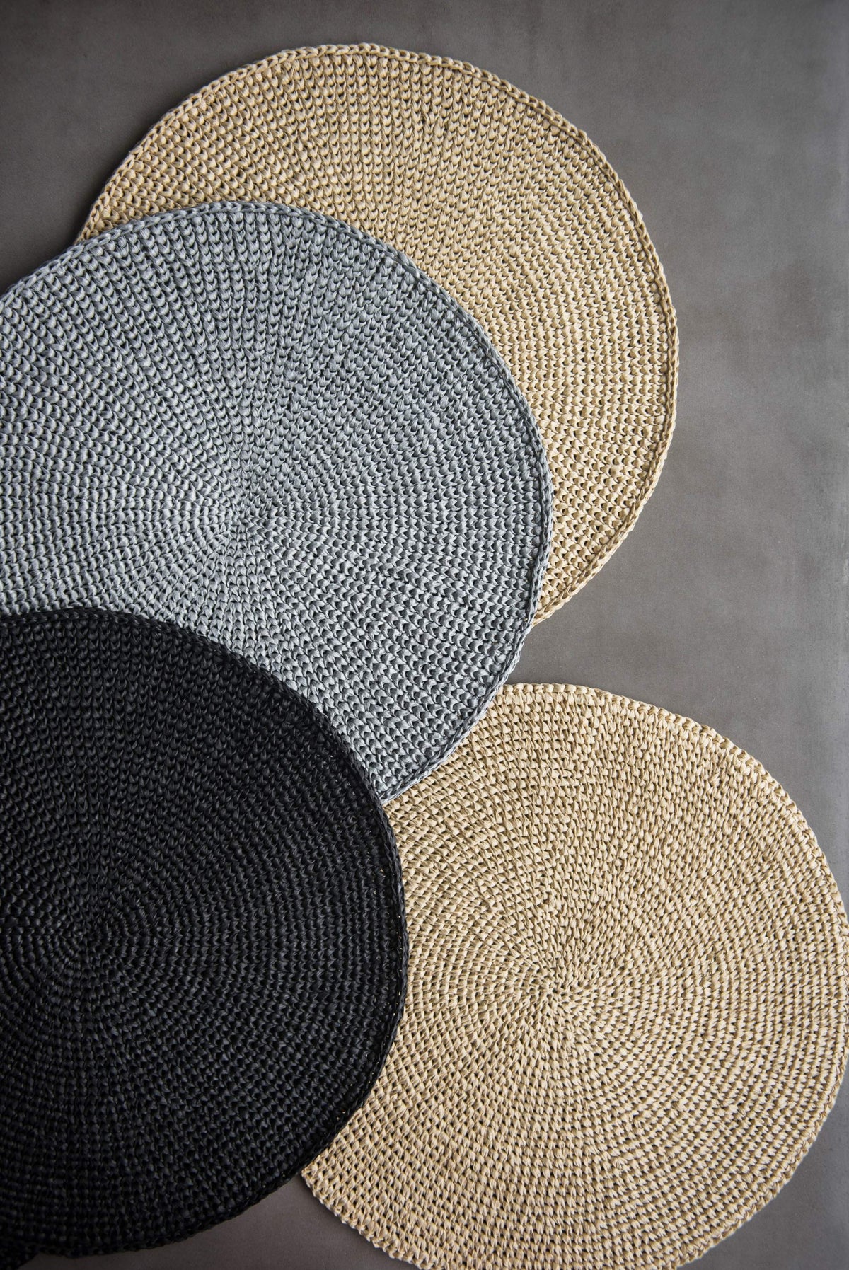 Round Raffia Placemats in natural beige, silver gray, and black raffia, hand-crocheted in a round spiral weave