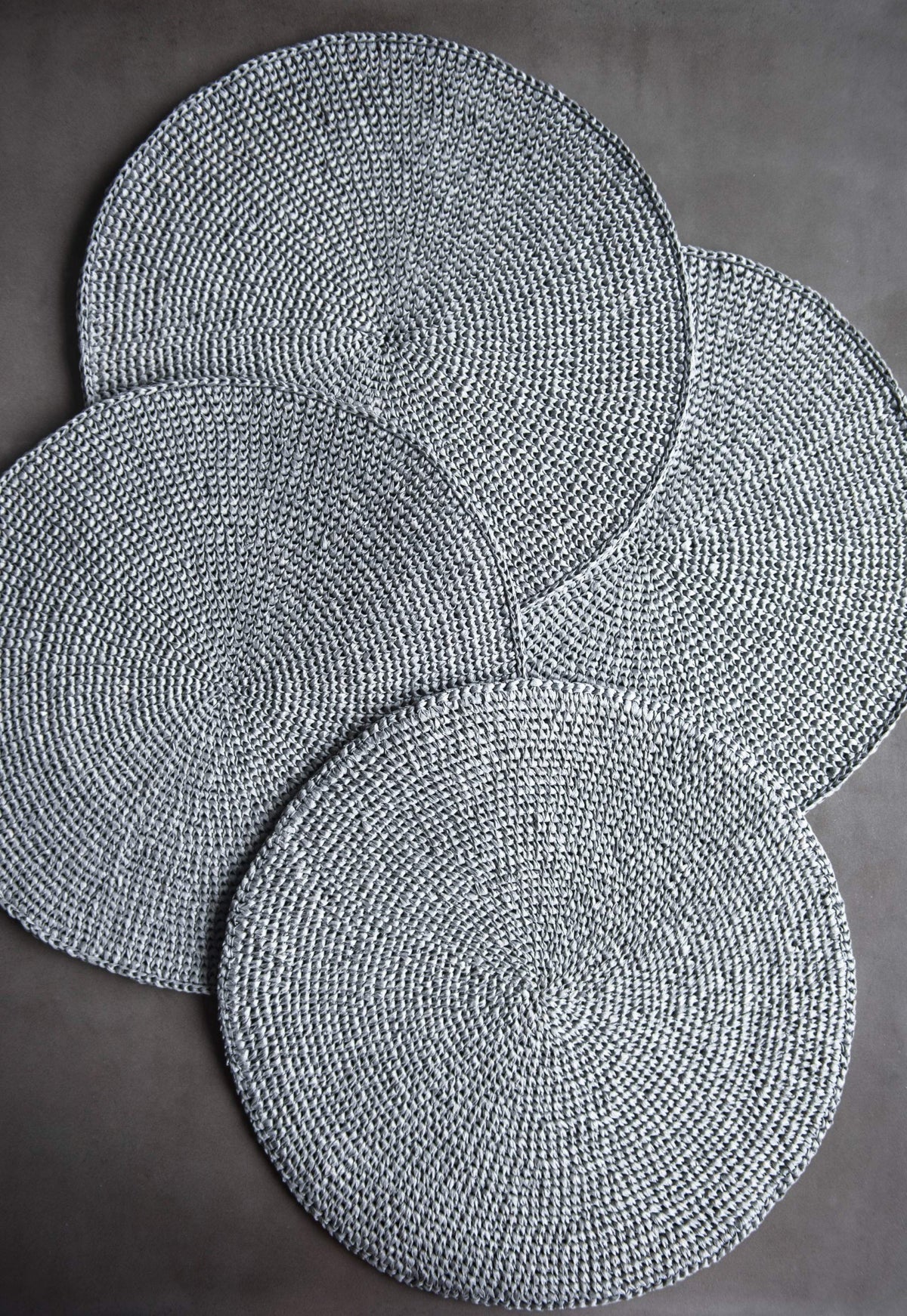 Round Raffia Placemats in silver gray raffia, hand-crocheted with a textured spiral weave and rounded edges.