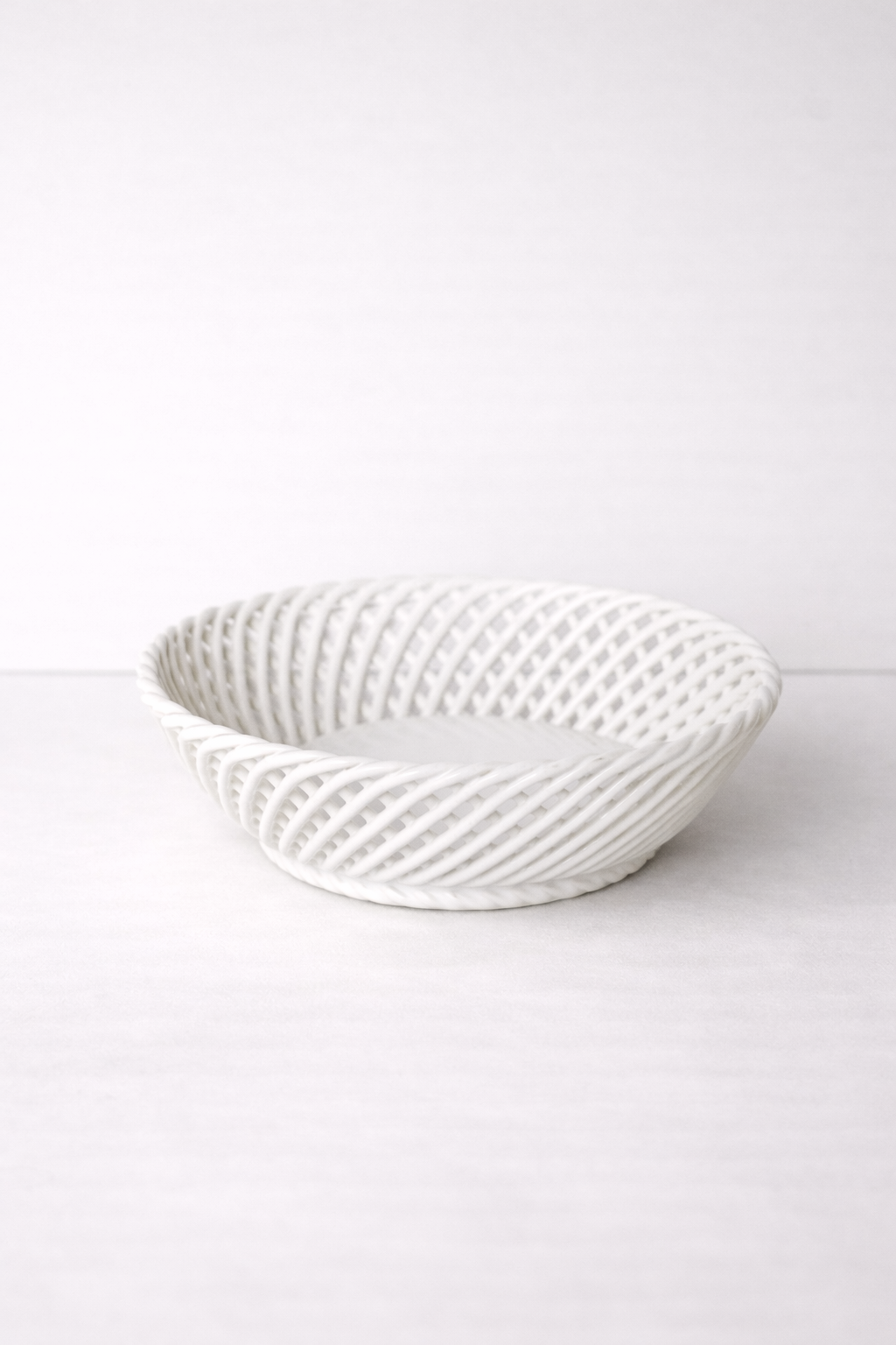 Ceramic Round Hand-Woven Basket in glossy white porcelain, with an airy interlaced weave and shallow round shape.