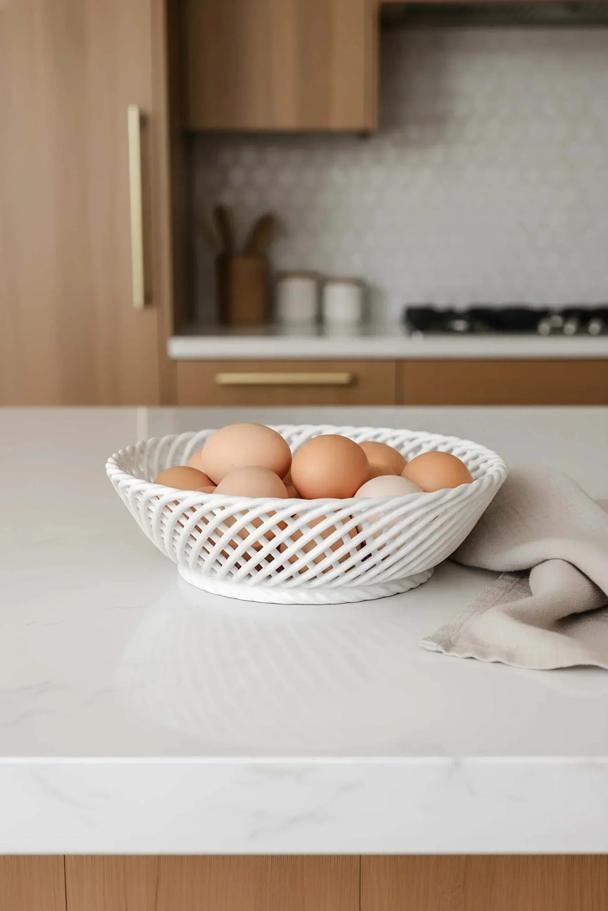 Ceramic Round Hand-Woven Basket in glossy white porcelain, with an open crisscross weave and a shallow round shape holding eggs.