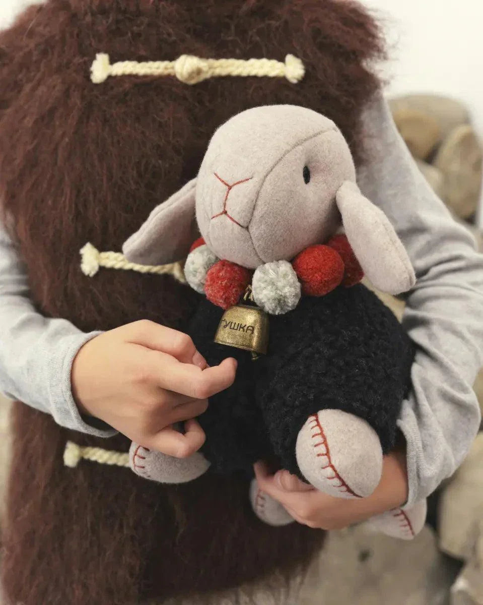 Wool Lamb Toy with a pale gray wool face, black curly fleece body, stitched features, and red and cream bead collar.