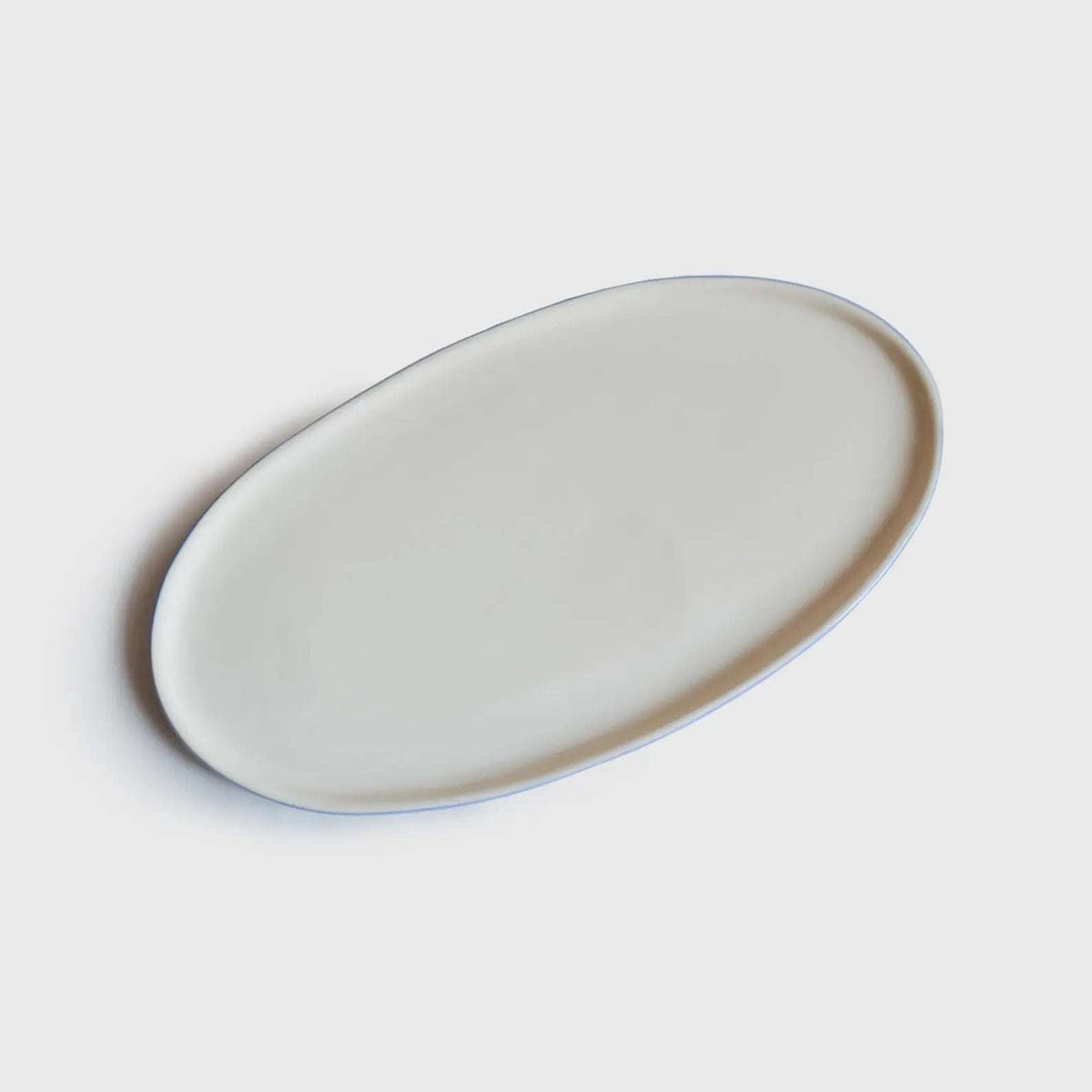 Porcelain Serving Platter with an oval shape, smooth pale glazed interior, and subtle blue exterior rim.